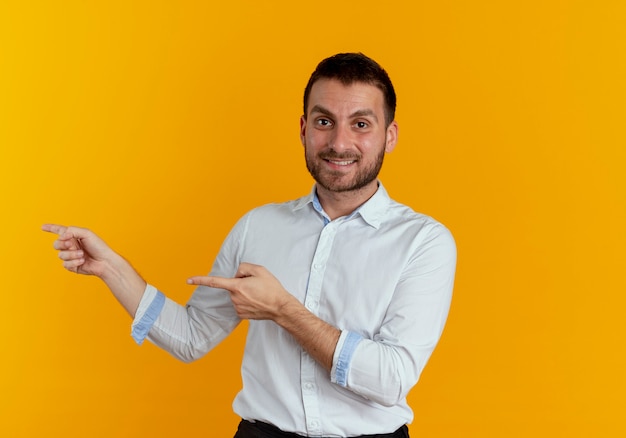 Smiling handsome man points at side with two hands isolated on orange wall