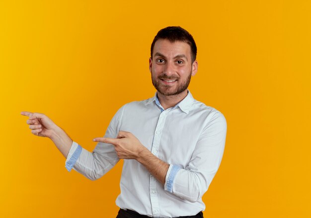 Smiling handsome man points at side with two hands isolated on orange wall