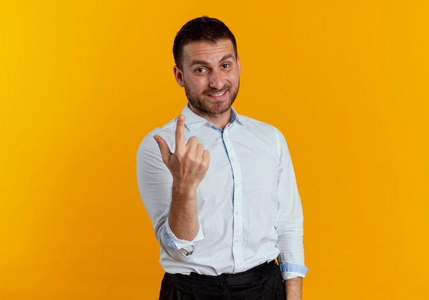 Smiling handsome man points up isolated on orange wall