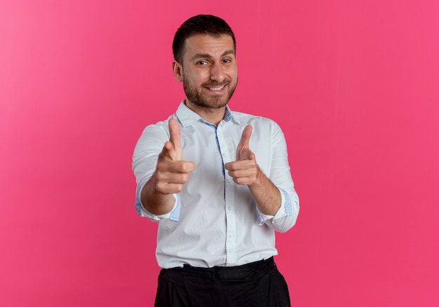 Smiling handsome man points with two hands isolated on pink wall