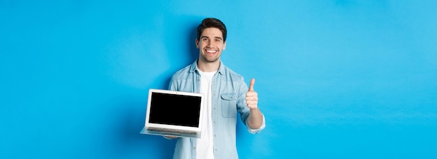 Free photo smiling handsome man showing laptop screen and thumbup like promo offer recommending website standin