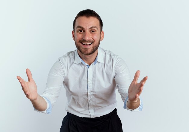 Smiling handsome man stands with raised hands and looks isolated on white wall