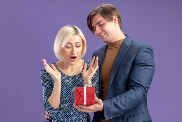 Free photo smiling handsome slavic man giving red gift box to surprised pretty blonde woman on valentine's day