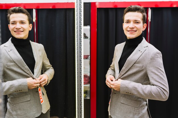 Smiling handsome young man trying jacket in front of mirror