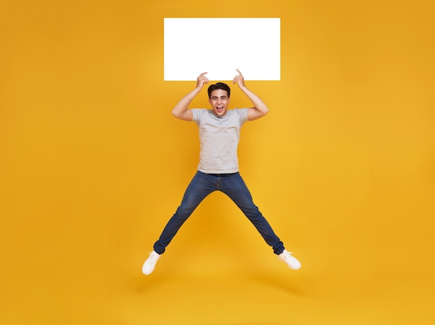 Smiling happy Asian man jumping and holding blank speech bubbles on yellow background advertise announcement concept