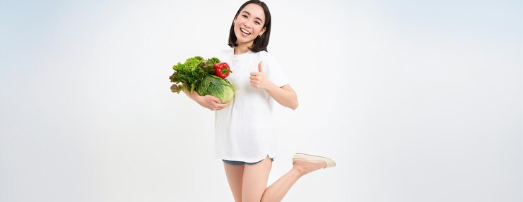 무료 Photo 웃는 행복한 아시아 여성은  바탕에 고립된 건강한 원시 음식을 먹는 이와 채소를 보여줍니다.
