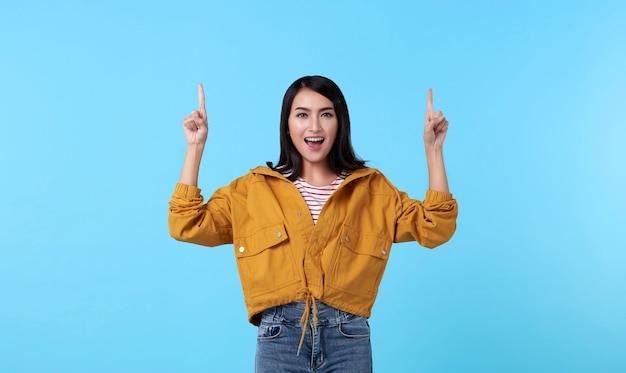 Smiling happy asian woman with her finger pointing isolated on light blue banner background with copy space.