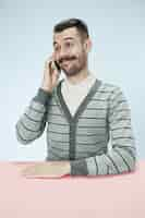 Free photo smiling happy business man talking on phone sitting at the table. concept of male emotions