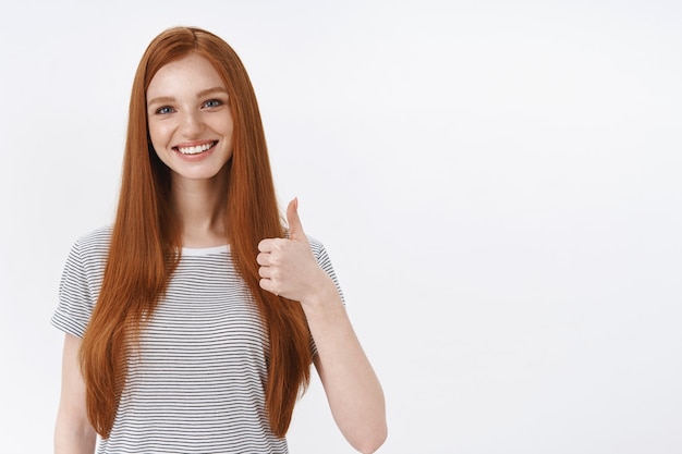 Smiling happy ginger girl student show thumb up smiling delighted recommend proudly good product, agree like good meal, approve interesting concept, white wall