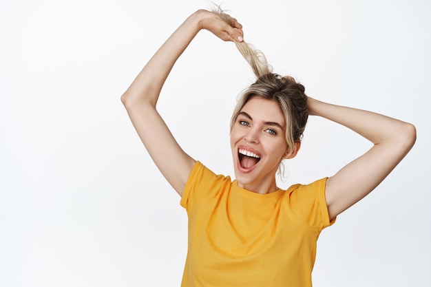 Smiling happy girl pull her hair and laughing, concept of healthy and stong hair, haircare product and cosmetics advertising, standing in yellow t-shirt on white