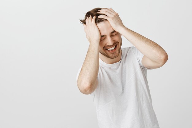 Smiling happy man can't believe own luck, holding hands on head and laughing