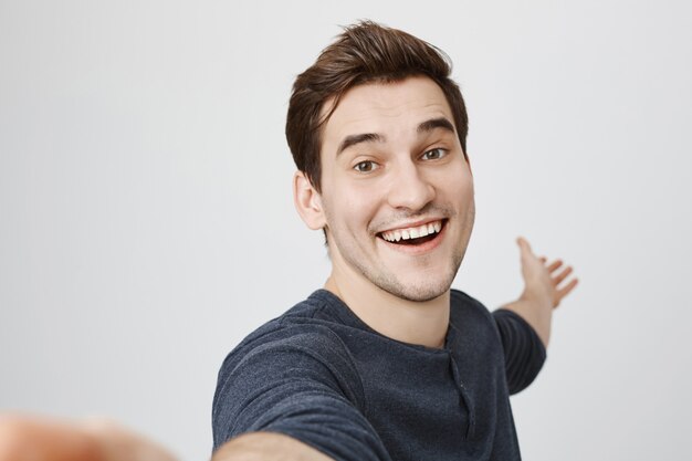 Smiling happy man taking selfie and pointing hand