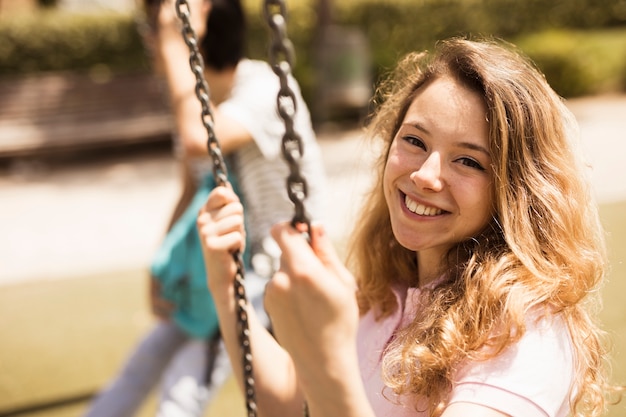 Smiling happy schoolgirl sitting on swings