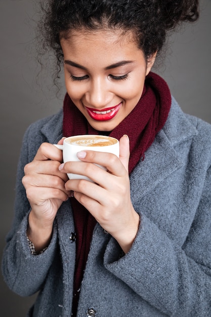 一杯のコーヒーを保持しているコートで笑顔の幸せな女