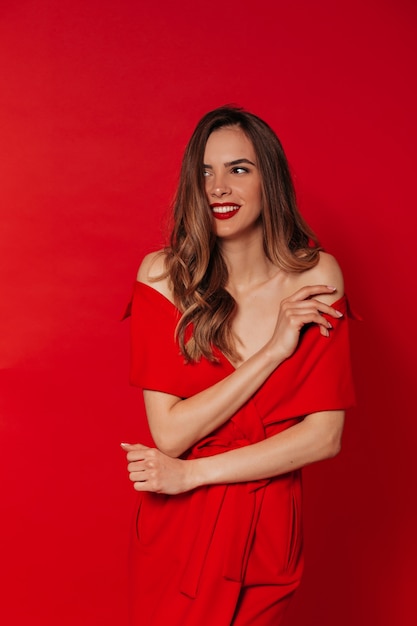 Smiling happy woman in red dress with red lips posing over red wall