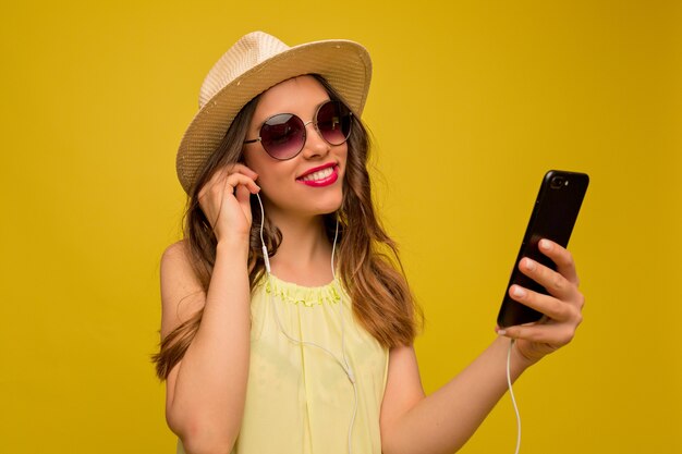 Улыбающаяся счастливая женщина в летней шляпе и солнцезащитных очках со смартфоном