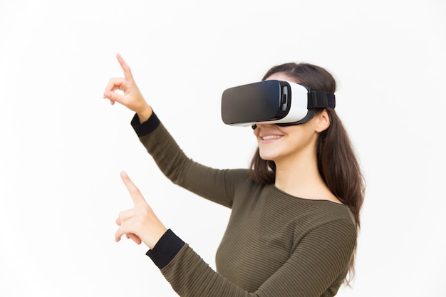 Smiling happy woman in VR headset touching air