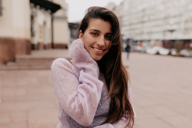 Smiling happy woman with long hair wearing violet sweater posing over old buildings