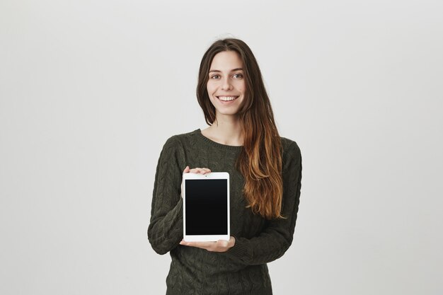 デジタルタブレットの画面を見せて幸せな若い女の笑顔、アプリやショップを宣伝