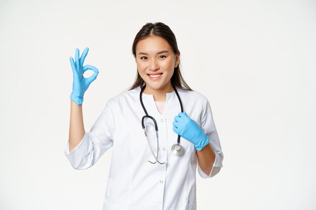 고무 장갑과 의료 유니폼을 입은 웃는 의료 종사자 아시아 여성 의사는 승인 확인을 보여줍니다...