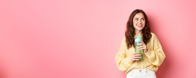 Sorridente ragazza bruna sana e sportiva che sembra premurosa da parte al logo che tiene una bottiglia d'acqua con