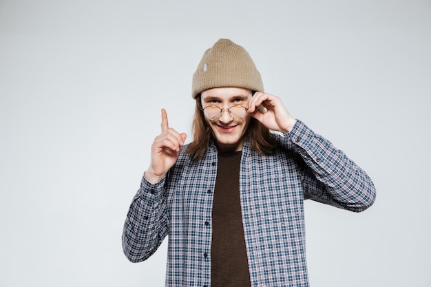 Smiling hipster in eyeglasses pointing up