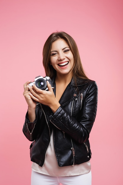 カジュアルな服装で笑顔の流行に敏感な女性は古いカメラを保持します。