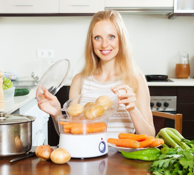 Smiling  housewife cooking potatoes with electric steamer