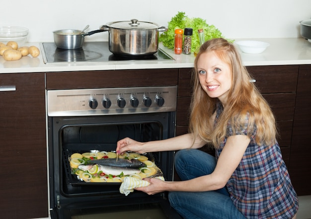 Smiling housewife cooking saltwater fish and potatoes on sheet pan