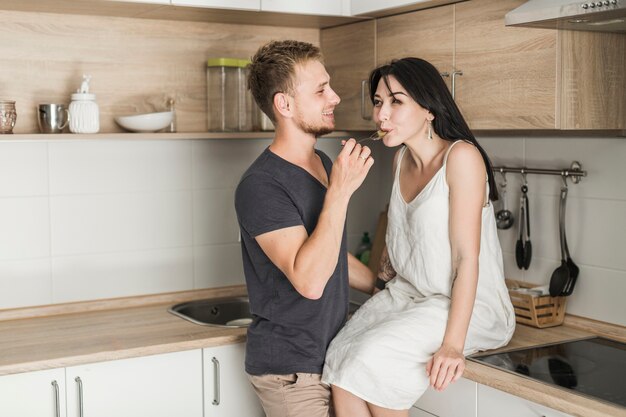 Улыбающийся муж кормления пищи его жена, сидя на кухне счетчик