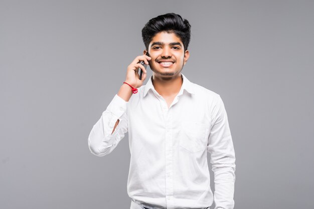 Smiling indian businessman calling on smartphone over grey wall