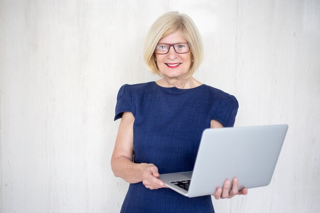 Smiling intelligent senior woman holding laptop