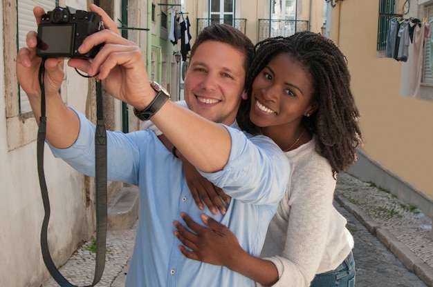 Smiling interracial couple taking selfie photo in street