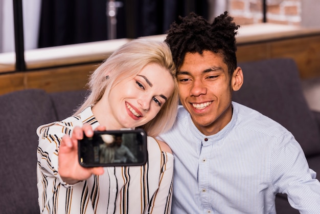 Giovani coppie interrazziali sorridenti che prendono selfie sullo smartphone