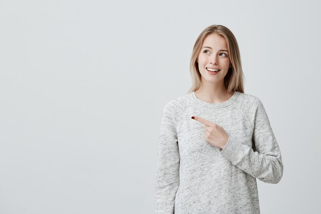 Smiling joyful woman pointing with finger at copyspace