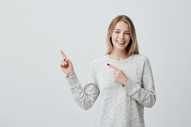 Smiling joyful woman pointing with finger at copyspace