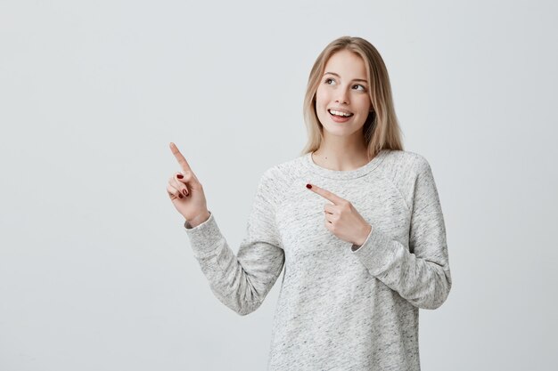 Smiling joyful woman pointing with finger at copyspace
