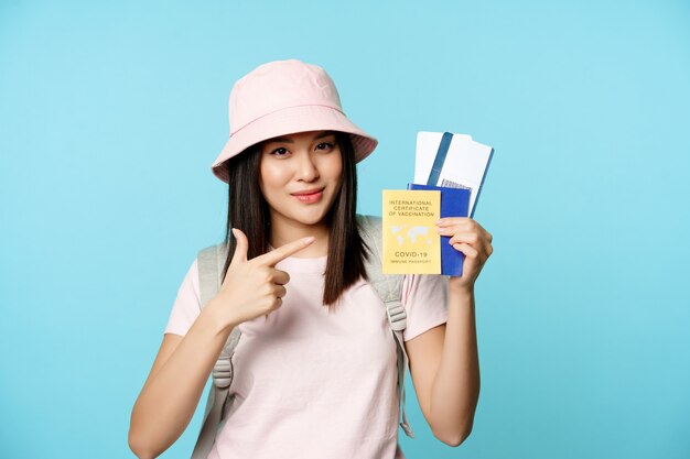 Smiling korean tourist shows her passport vaccination certificate from coronavirus disease getting v...