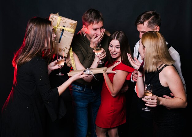 Smiling ladies and amazed guys with glasses of drinks and present boxes