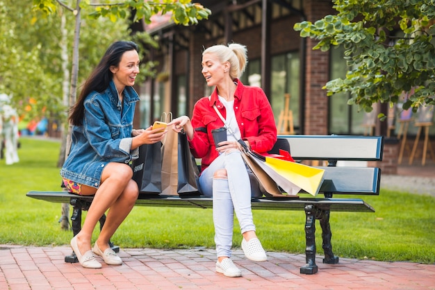 Smiling ladies looking at smartphone on bench