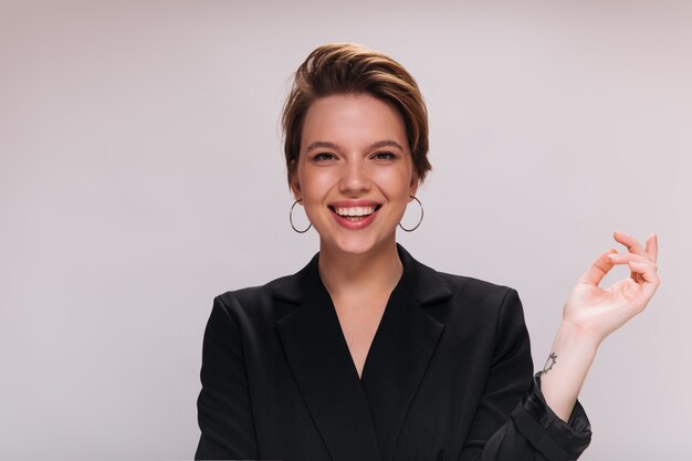 Smiling lady in black jacket posing on isolated background. Happy cheerful woman in dark suit laughing and looking into camera