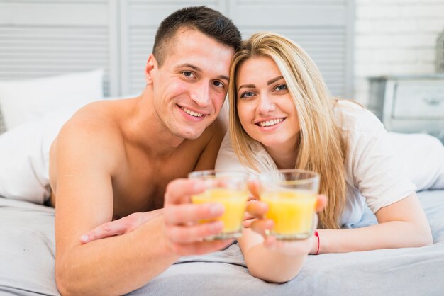 Smiling lady and guy with glasses of juice in bed