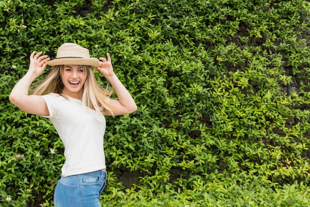 Foto gratuita signora sorridente in cappello vicino al cespuglio verde