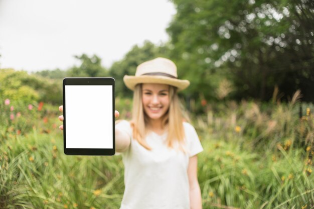 草の近くのタブレットを示す帽子の笑顔の女性