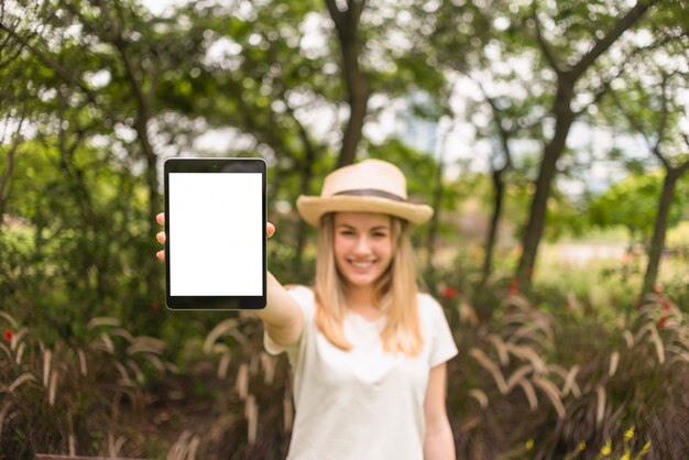 Smiling lady in hat showing tablet in park