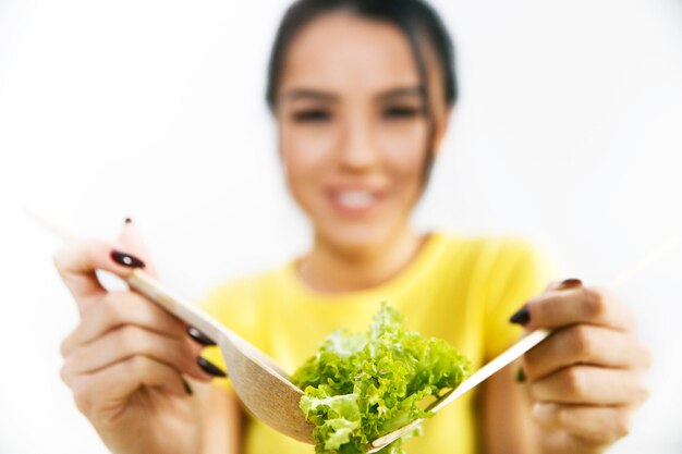 笑顔の女性はスプーンで緑のサラダを保持しています