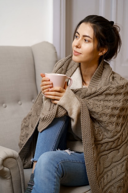 無料写真 スマートな流行の服を着た笑顔の女性は、お茶を片手に肘掛け椅子に座っています。