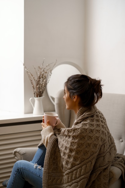 無料写真 スマートな流行の服を着た笑顔の女性は、お茶を片手に肘掛け椅子に座っています。