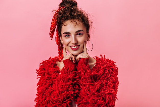 La signora sorridente in vestito rosso esamina la macchina fotografica su fondo rosa