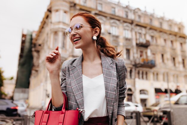 スタイリッシュな眼鏡の笑顔の女性は赤いバッグを保持します